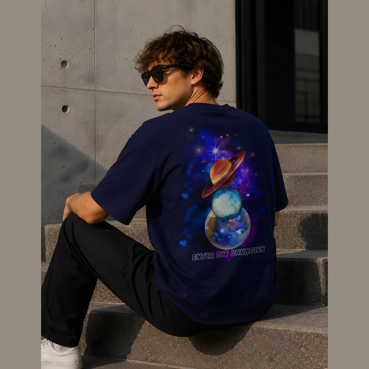 Person wearing a blue t-shirt with a space-themed design sitting on steps.