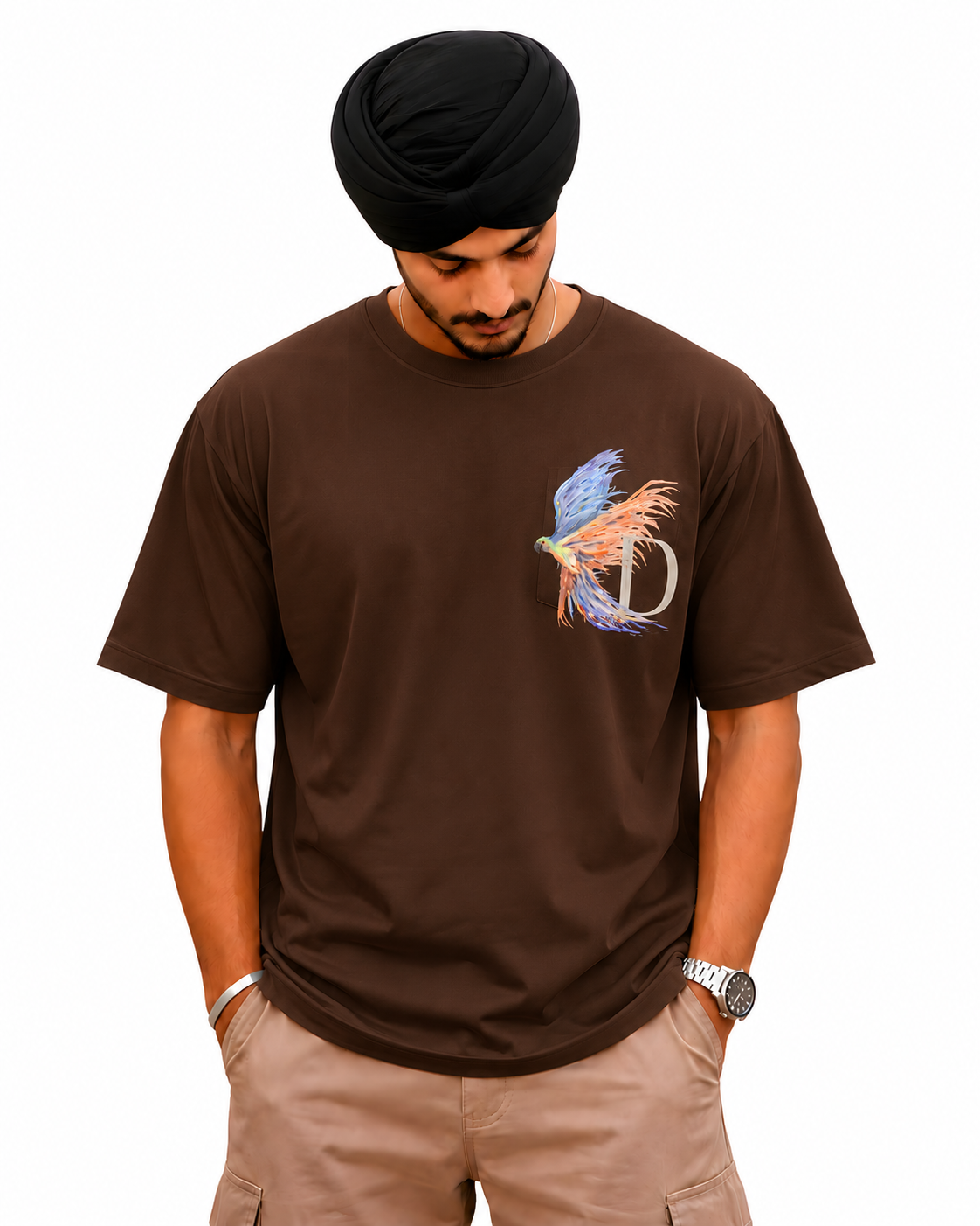 A man wearing a brown short-sleeve t-shirt with a colorful bird and 'D' graphic on the chest, paired with khaki cargo pants and a black turban, against a plain white background.