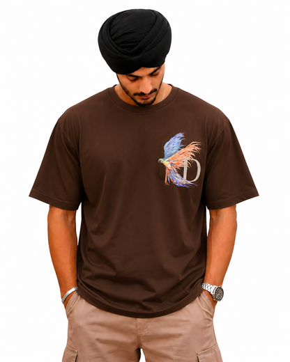 A man wearing a brown short-sleeve t-shirt with a colorful bird and 'D' graphic on the chest, paired with khaki cargo pants and a black turban, against a plain white background.