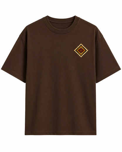A dark brown short-sleeve crewneck t-shirt with a small diamond-shaped embroidered patch on the left chest, displayed against a solid white background.