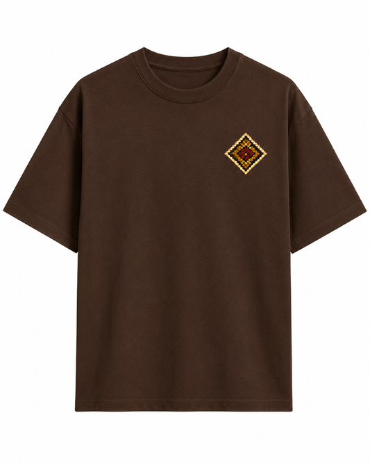 A dark brown short-sleeve crewneck t-shirt with a small diamond-shaped embroidered patch on the left chest, displayed against a solid white background.